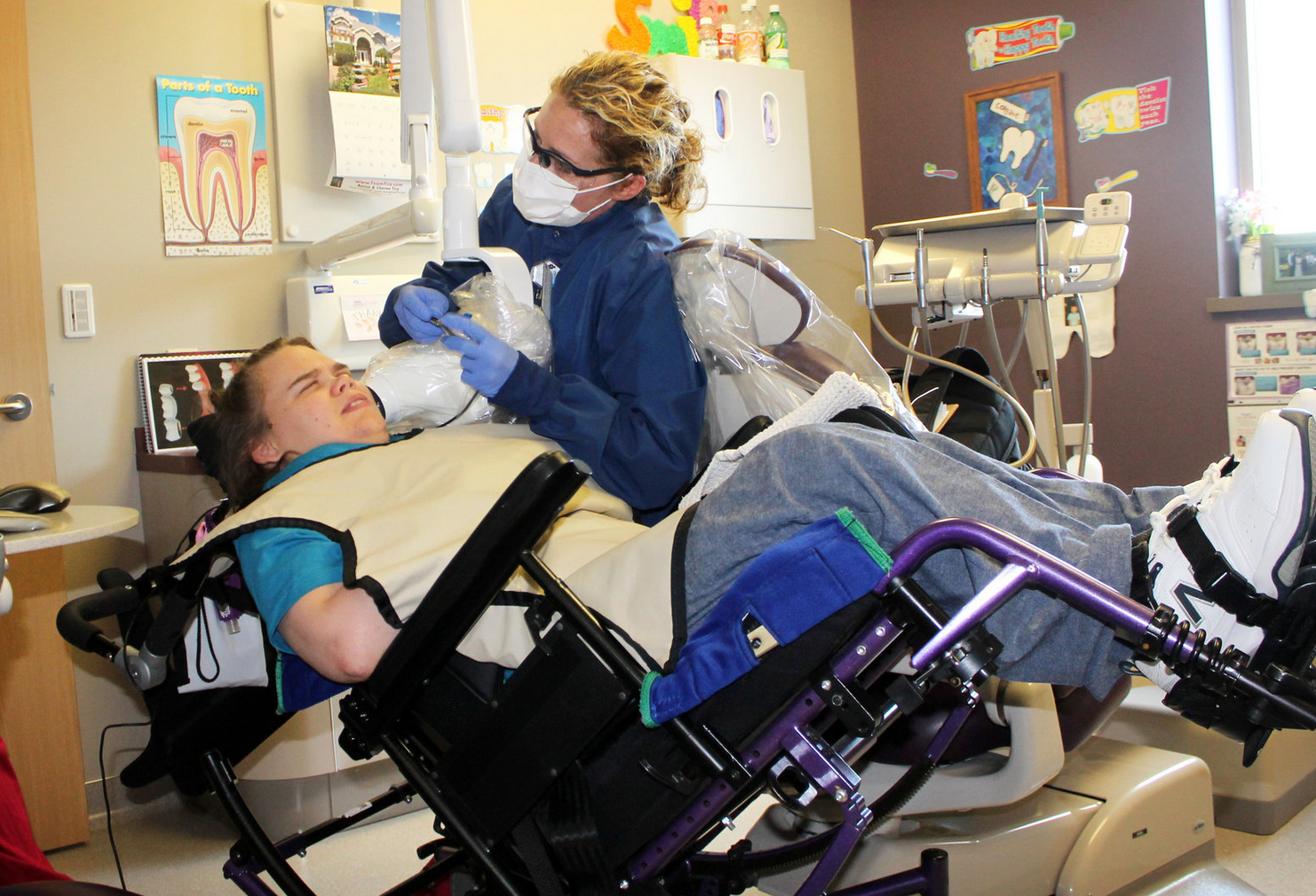 Teenager in a wheelchair having his mouth examined in a dental clinic by a dentist who is wearing a mask