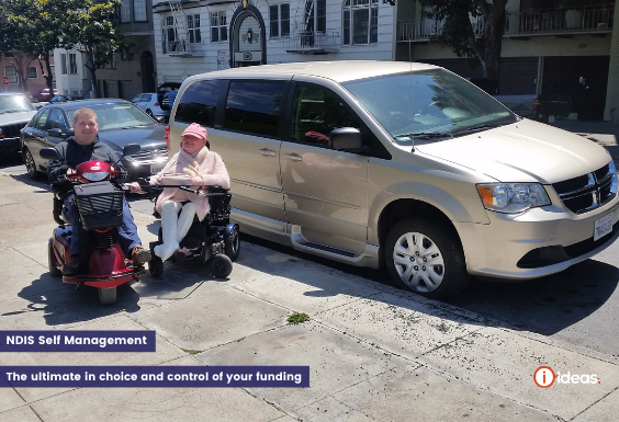 A couple infront of an accesible vehicle in San Fransisco, they are both seated, Carolyn in a wheelchair, Steve in an motorised scooter 