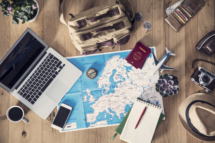 A travel concept flatlay with map, computer, passport, phone, notebook and camera