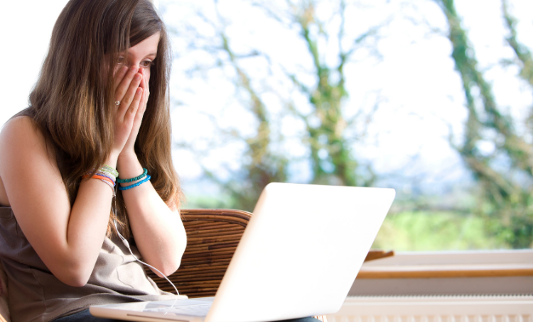 A girl with her hands covering her mouth in surprise or shock, She looks at a laptop.