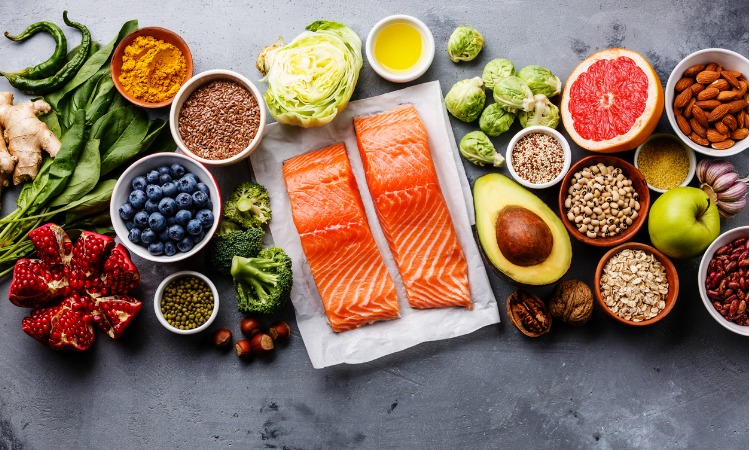 Image of healthy food, including vegetables, fruit and salmon, all laid out on a grey benchtop.