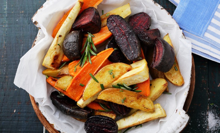 A plate of baked vegetables, carrot, beetroot potato, with some rosemary sprinkled on top.