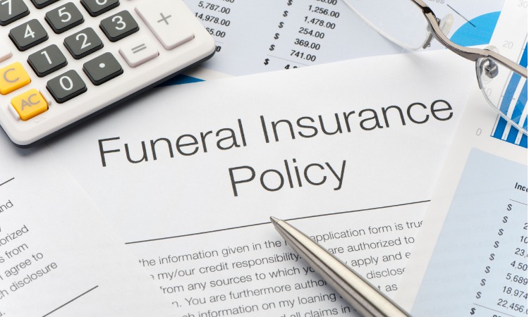 Close up of funeral insurance policy papers, with a silver pen and calculator in the corner.