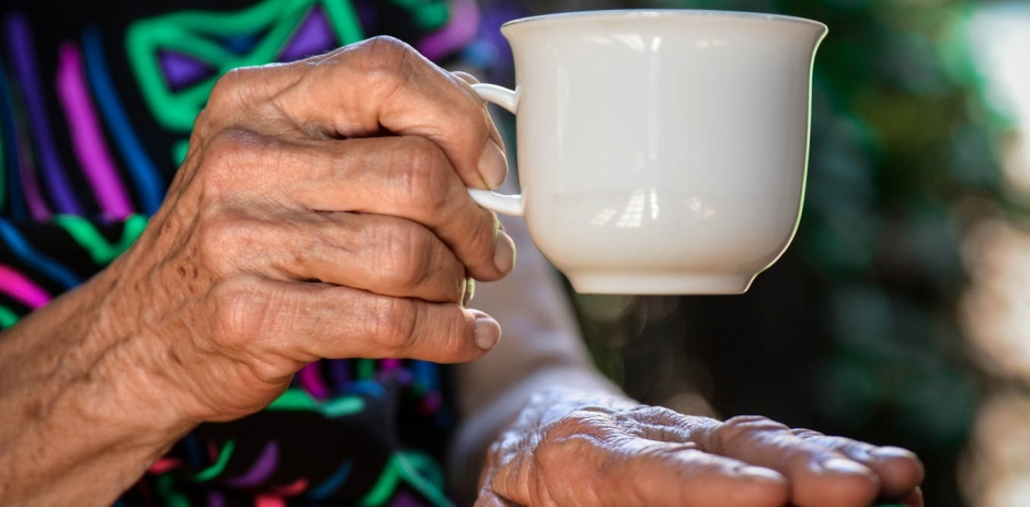 Image of an aged woman's hand holding a white cup