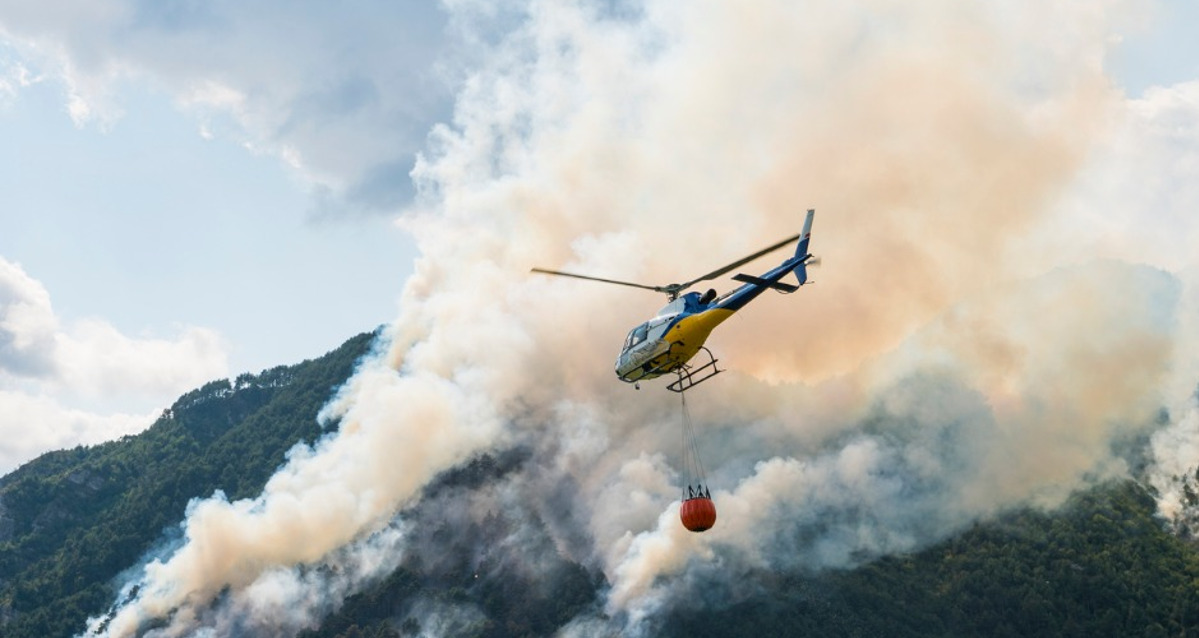 Image of a helicopter carrying a bucket of water near a bushfire.