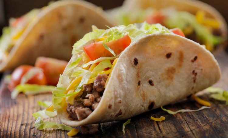 An image of taco's. A tortilla filled with mince, lettuce, cheese and tomato.