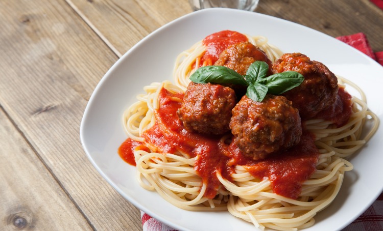 Four Italian meatballs on a bed of pasta and tomato based sauce, Plated and read to eat.