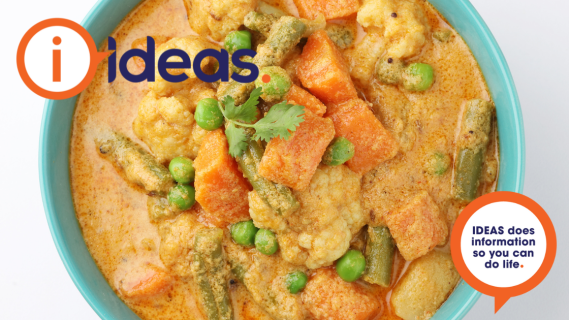A top down photo of a bowl of curry, with sweet potato, carrot, cauliflower, peas and beans.