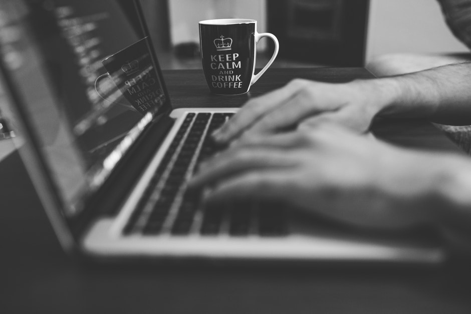 black and white image of hands typing on a laptop. a mug sits behind and reads "Keep Calm and Drink Coffee".