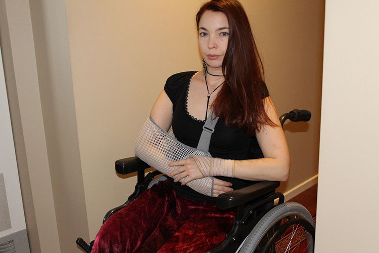 Woman in a wheelchair with her arm in a sling. 