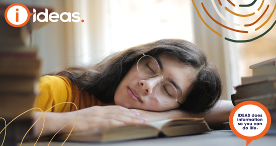tired woman with glasses sleeping with face on open book. IDEAS logo is in upper left corner.
