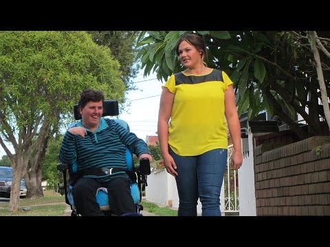 Lady in a wheelchair and a friend walking by her side on the footpath