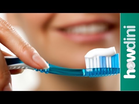 Toothbrush with toothpaste on it with a smiling lady behind it