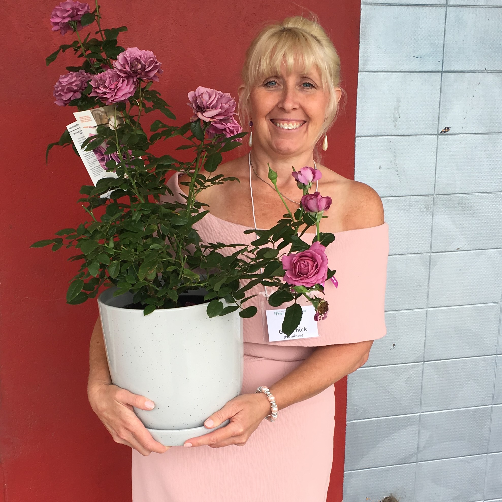A well dressed woman is holding a potted rose