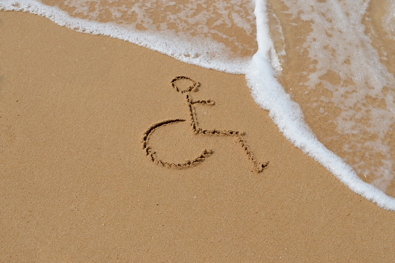 An outline of a wheelchair that has been drawn into the sand on a beach with water in the picture