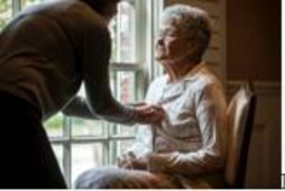 Older woman sits while being assisted to dress in an aged - care facility 