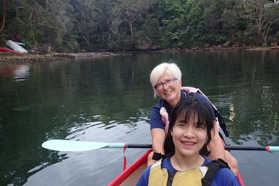 Two women sitting in a boat. Both are smiling and one is holding an oar.